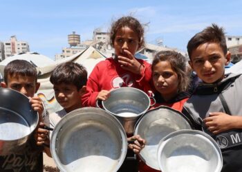 Children in Gaza waiting to have their empty containers filled with food. (Photo UN News)